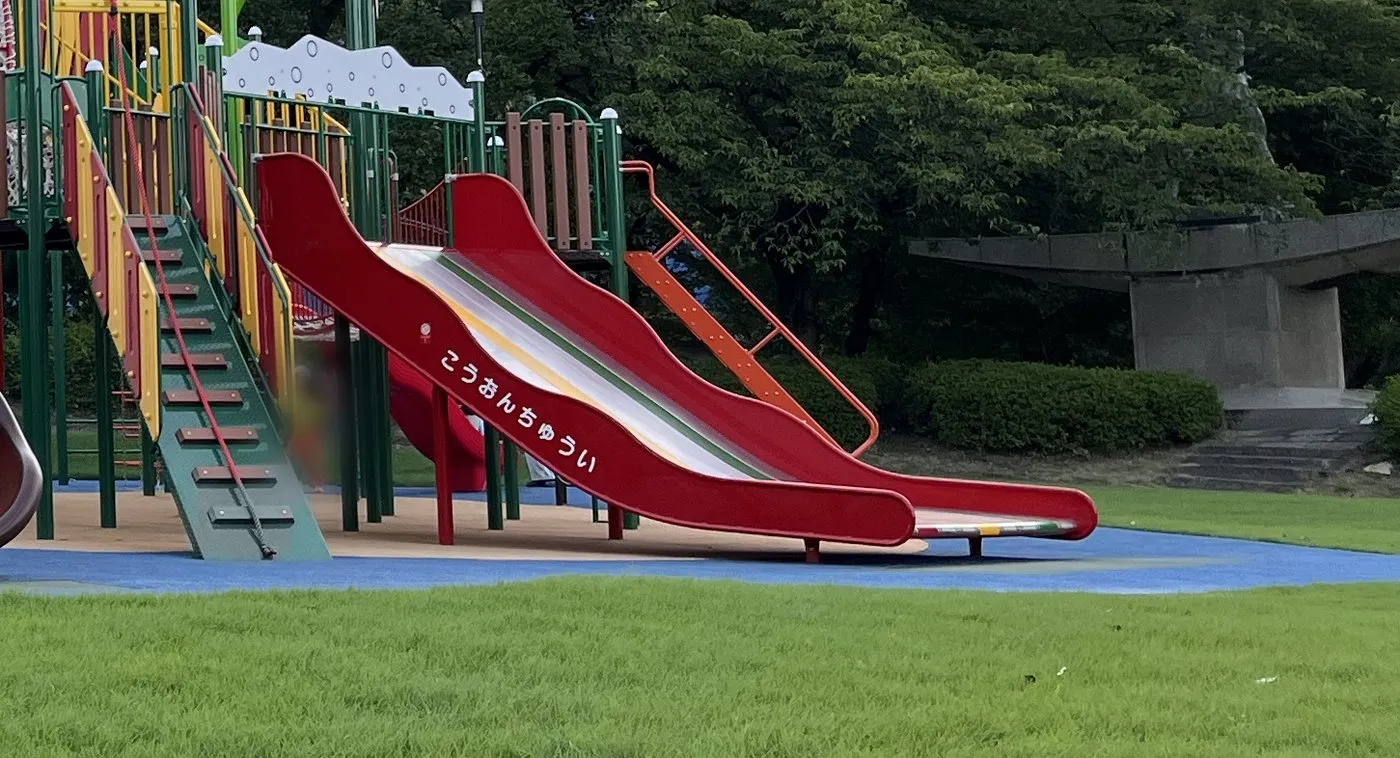 赤い長い滑り台の側面に、白いひらがなで「こうおんちゅうい」と書かれている